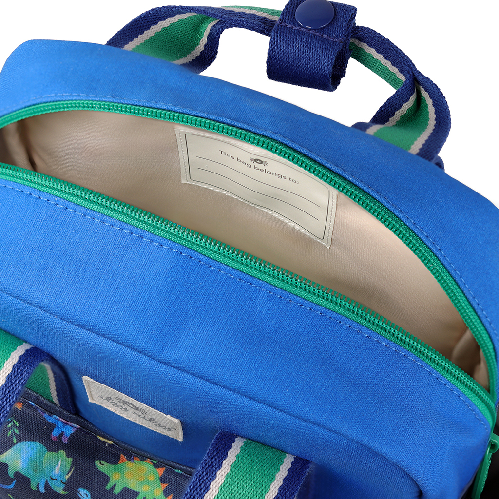 101601542 Itzy Bitzy Bag™ Toddler Backpack - Raining Dinos (4) The Itzy Ritzy Sweetie Strap Plus Bear Silicone Pacifier Clip showcases a stylish blue exterior with a green zipper and features a white interior label for personal information. The top of the backpack opens to reveal the main compartment.