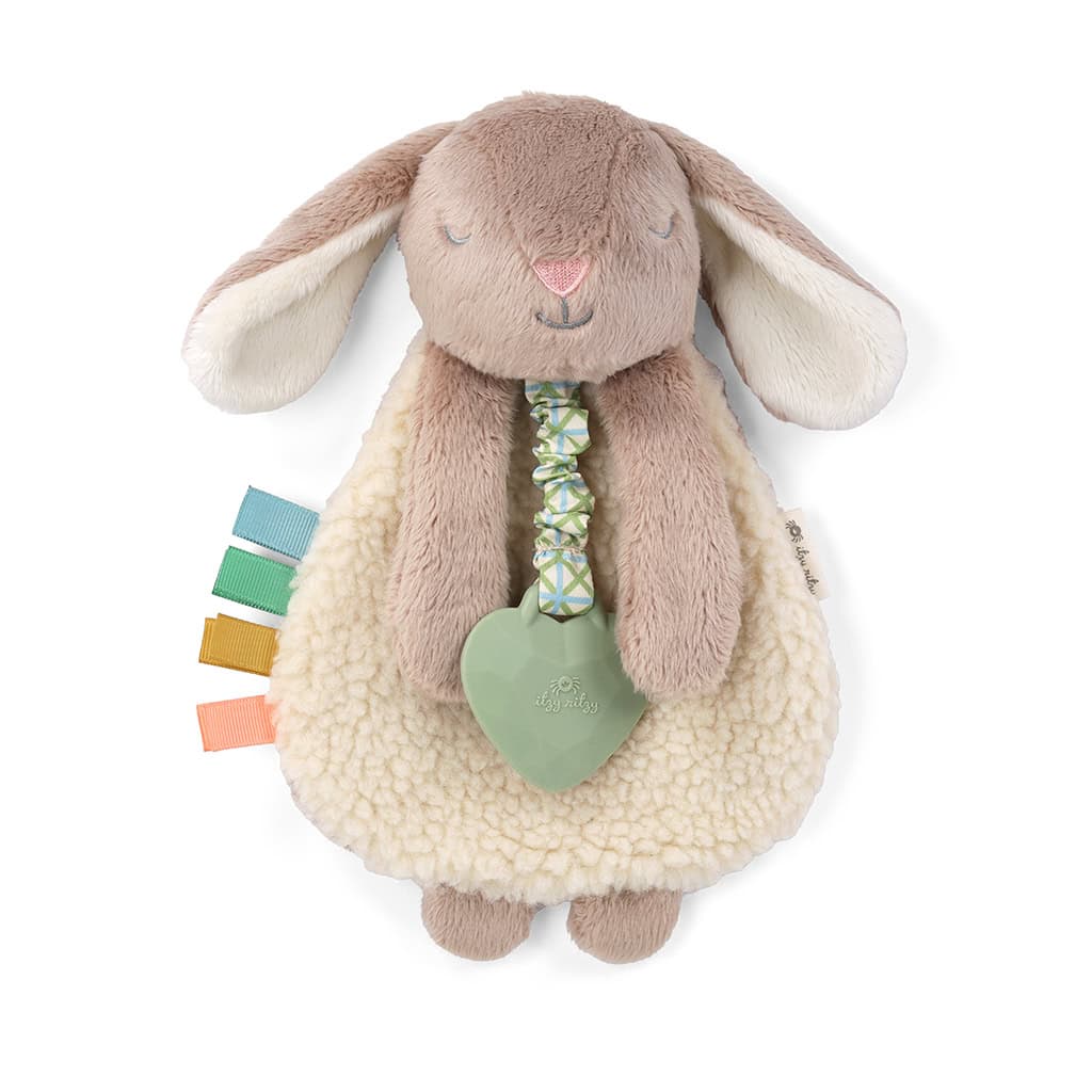 302801555 Itzy Lovey Taupe Bunny (2) A fluffy, beige-and-white stuffed rabbit toy with long ears, a soft body, colorful fabric tags, and a green heart-shaped teething ring attached.