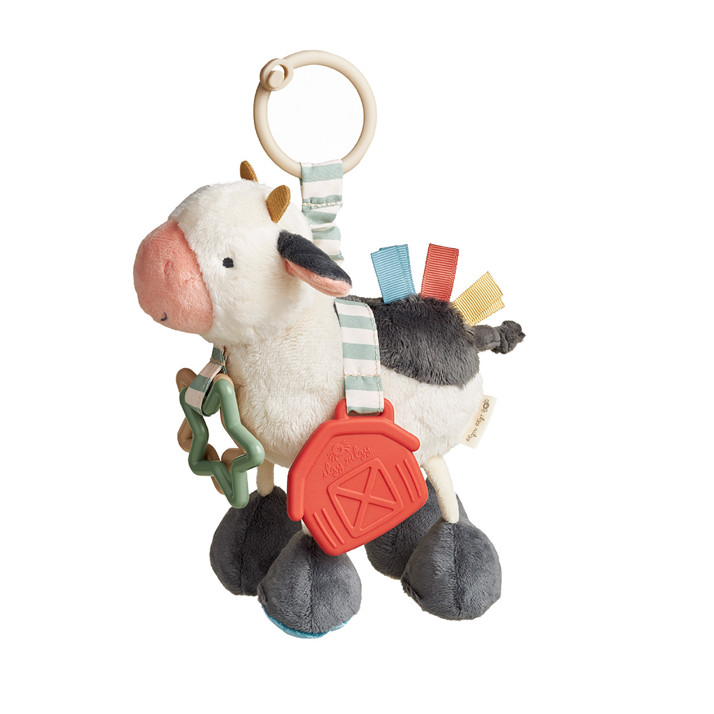 303201676_Itzy_Ritzy_Toy_Link_And_Love_Cow Plush cow toy with a teething ring and soft fabric tags, including a red barn and a star-shaped attachment.
