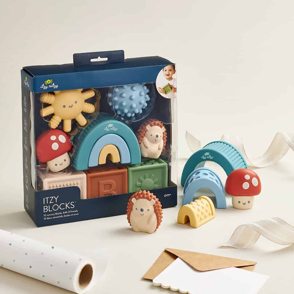 A set of colorful Itzy Ritzy Sensory Blocks 10-Piece Set featuring various shapes and textures, including a hedgehog and mushrooms, displayed with packaging on a neutral background.