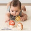 Infant lying on stomach on a carpet, reaching towards an Itzy Ritzy Sensory Blocks 10-Piece Set and a toy hedgehog.