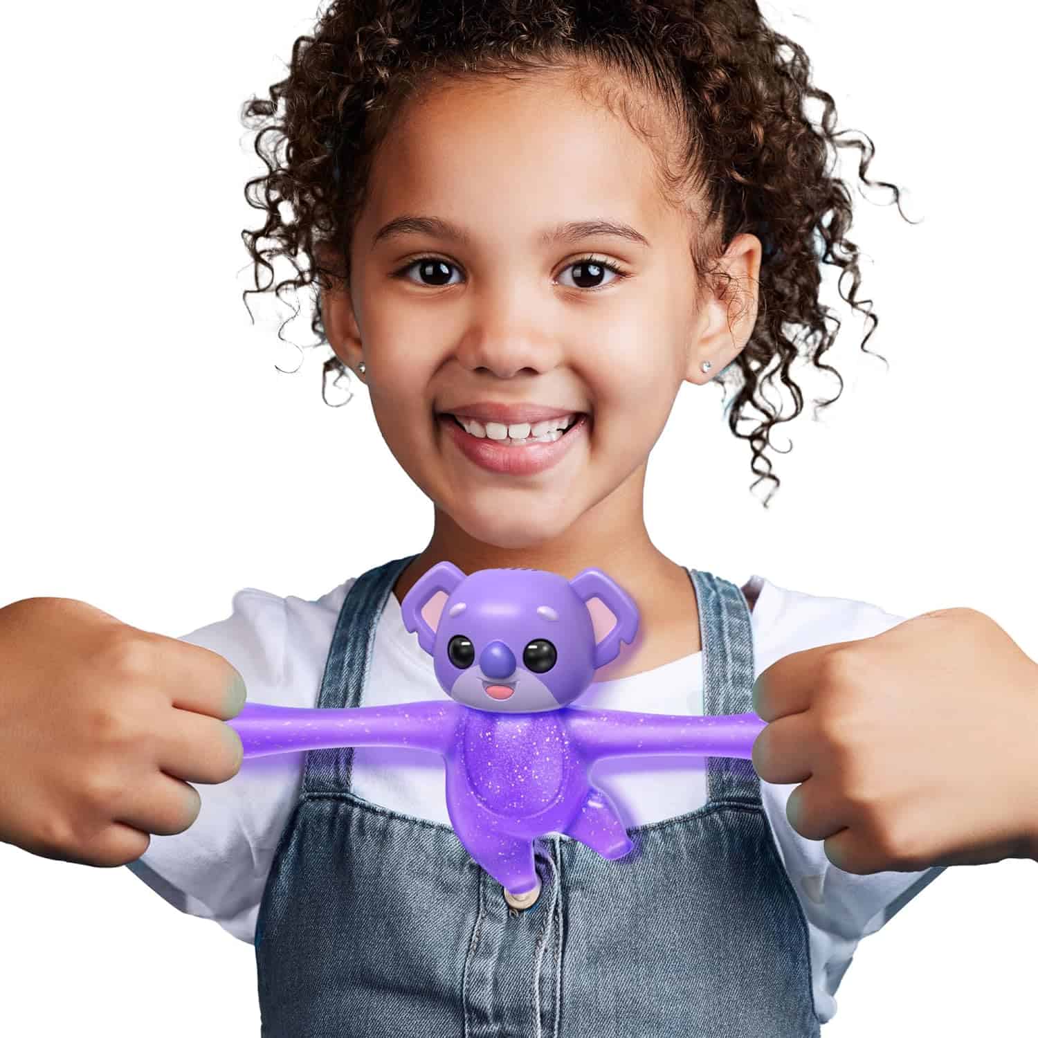Little Live Pets Hug n' Hang Zoogooz - Koomi Koala. an Interactive Electronic Squishy Stretchy Toy Pet with 70+ Sounds & Reactions. Stretch, Squish and Link Their Hands (3) A young girl smiles while holding a purple, stretchy toy shaped like a monkey with both hands.