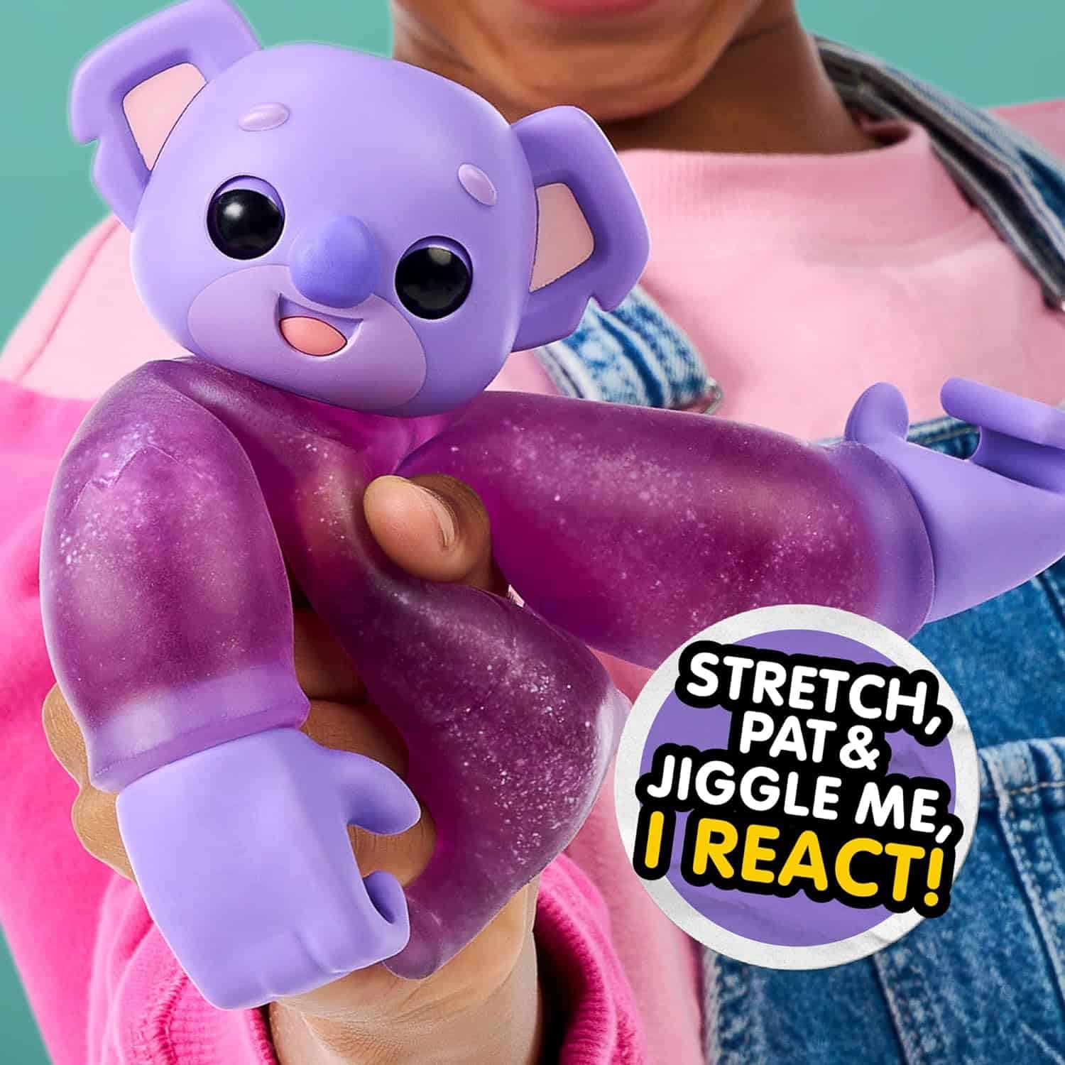 Little Live Pets Hug n' Hang Zoogooz - Koomi Koala. an Interactive Electronic Squishy Stretchy Toy Pet with 70+ Sounds & Reactions. Stretch, Squish and Link Their Hands (9) A person holds a purple koala toy with text beside it saying, "Stretch, pat & jiggle me, I react!" The toy has a smiling face and extended limbs.