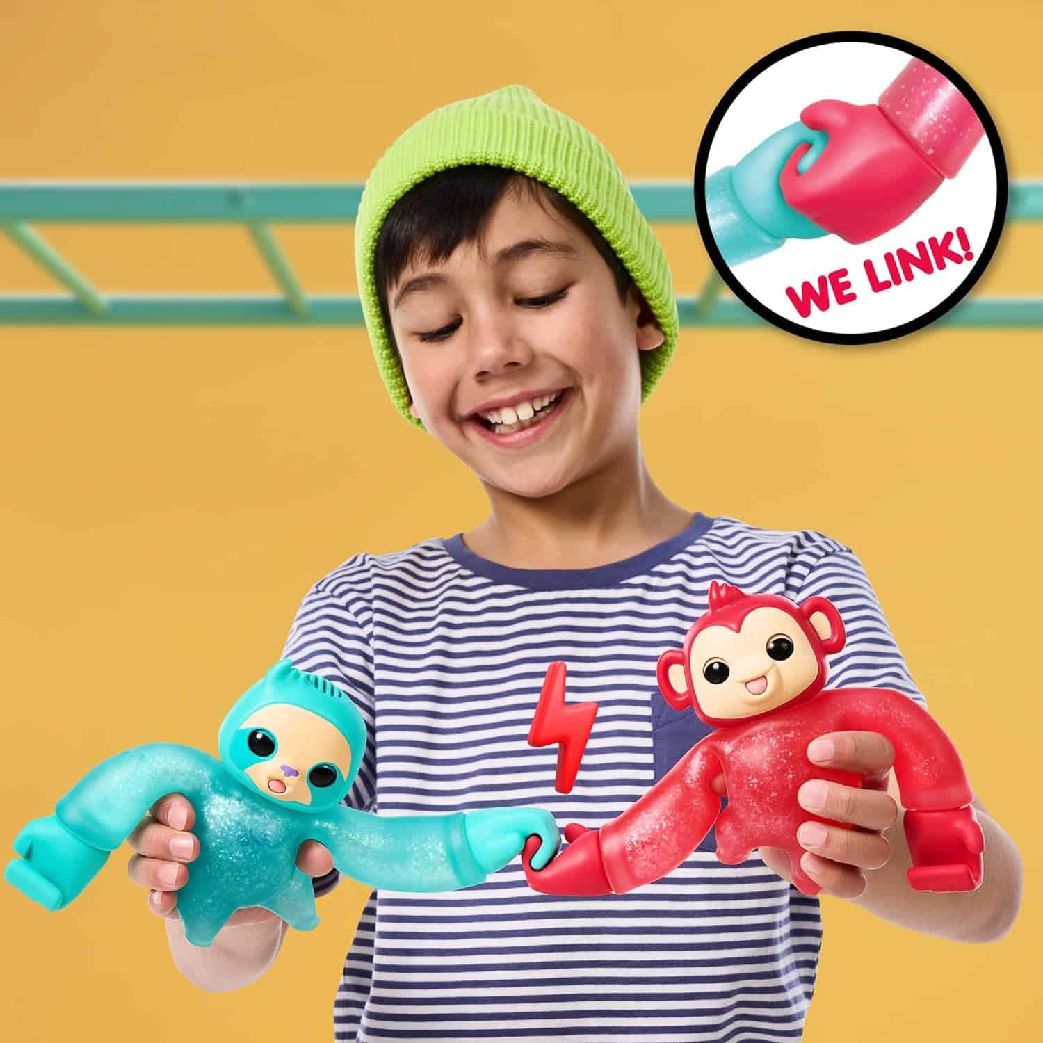 Little Live Pets Hug n' Hang Zoogooz - Mookie Monkey. an Interactive Electronic Squishy Stretchy Toy Pet with 70+ Sounds & Reactions. Stretch, Squish & Link Their Hands Medium (8) A child in a striped shirt and green beanie smiles while holding two colorful linking toys designed to connect at the hands. One toy is blue and resembles a sloth, the other is red and resembles a monkey.
