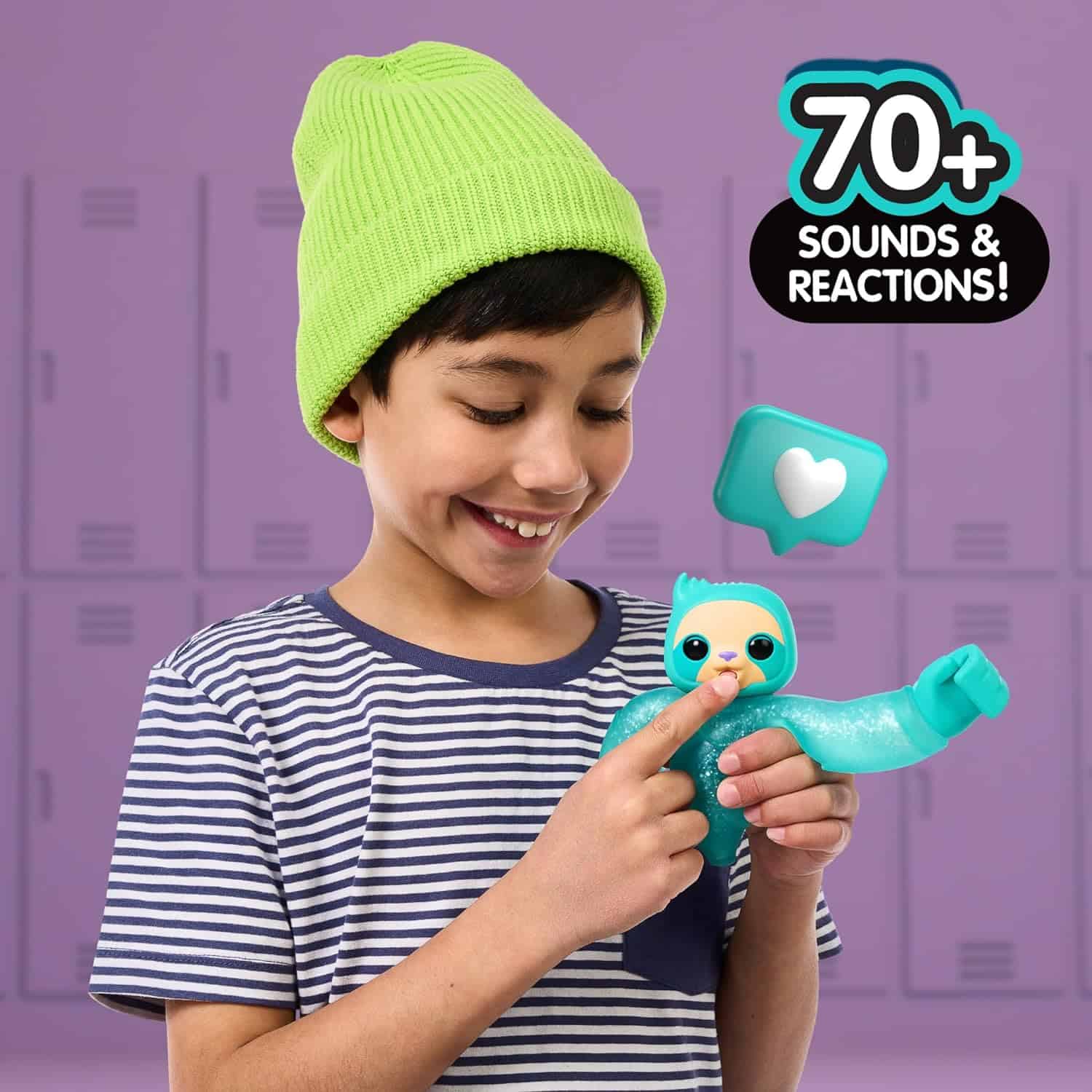 Little Live Pets Hug n' Hang Zoogooz - Sensoo Sloth. an Interactive Electronic Squishy Stretchy Toy Pet with 70+ Sounds & Reactions. Stretch, Squish and Link Their Hands (10) A young boy wearing a green beanie and striped shirt holds a blue interactive toy sloth. Text reads "70+ sounds & reactions!" with a heart icon. Lockers are visible in the background.