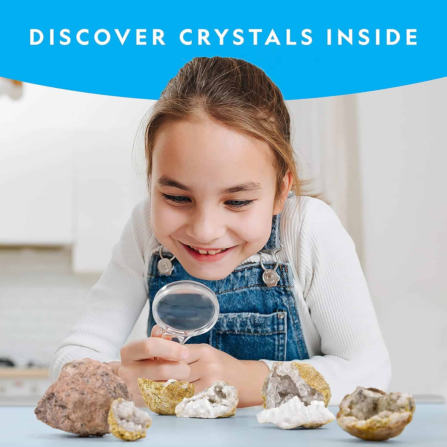 NATIONAL GEOGRAPHIC Break Open 10 Premium Geodes (6) A young girl examines rock geodes with a magnifying glass on a table. The text at the top reads "DISCOVER CRYSTALS INSIDE." Several open geodes revealing crystals are spread out in front of her. National Geographic Break Open 10 Premium Geodes