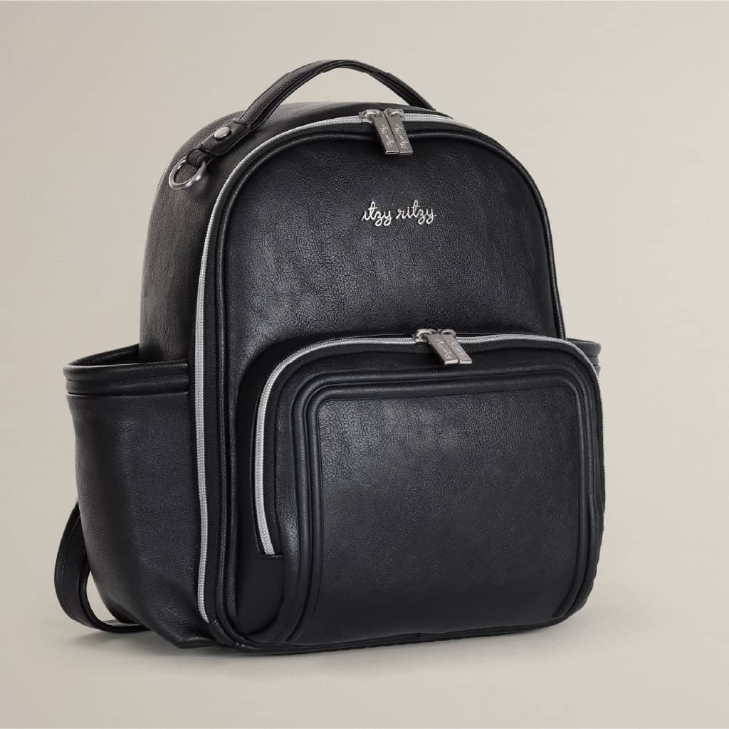 itzy-ritzy-101401619-itzy-mini-plus-backpack-noir-11 A black leather backpack with multiple zippered compartments and the brand name "Itzy Ritzy" embroidered on the front in white text.