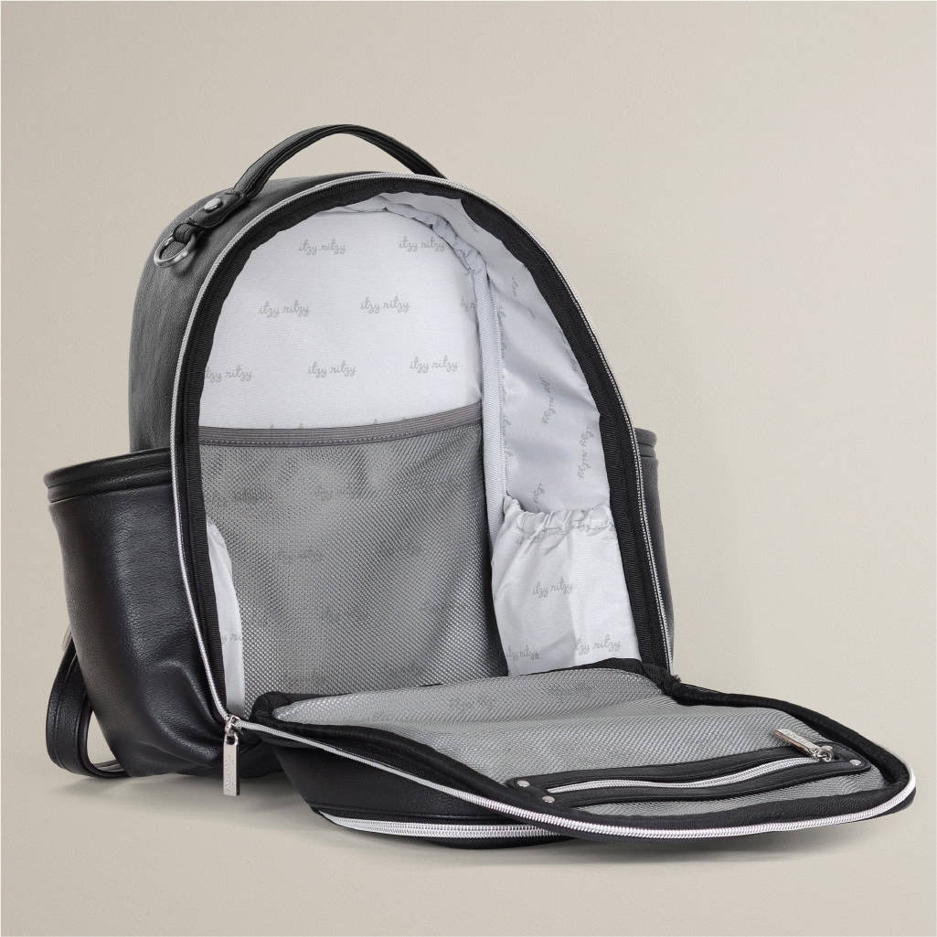 itzy-ritzy-101401619-itzy-mini-plus-backpack-noir-12 Image of an open black leather backpack showing its interior compartments, including a mesh pocket, a zipper pocket, and an elastic pocket. The inside lining has a repeating pattern of small text.