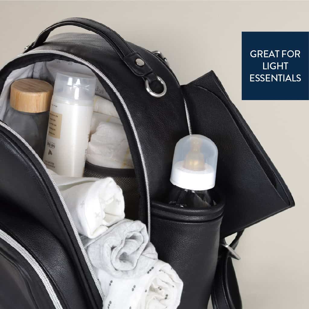 itzy-ritzy-101401619-itzy-mini-plus-backpack-noir-4 A black backpack is shown with its main compartment open, revealing a baby bottle, rolled clothes, and various small containers. A side pocket holds another baby bottle. Text reads "GREAT FOR LIGHT ESSENTIALS.
