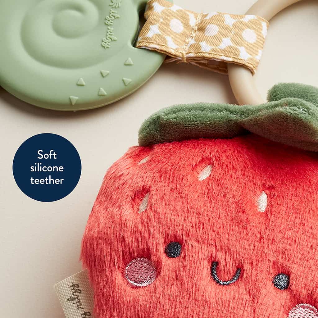 231220_Itzy_Ritzy_Digital_Shelf_ItzyPalStrawberry A soft silicone teether shaped like a red strawberry with a smiling face, paired with a green leaf and a polka dot bow handle called Itzy Ritzy - Itzy Pal - Plush Pal Infant Toy with Silicone Teether.