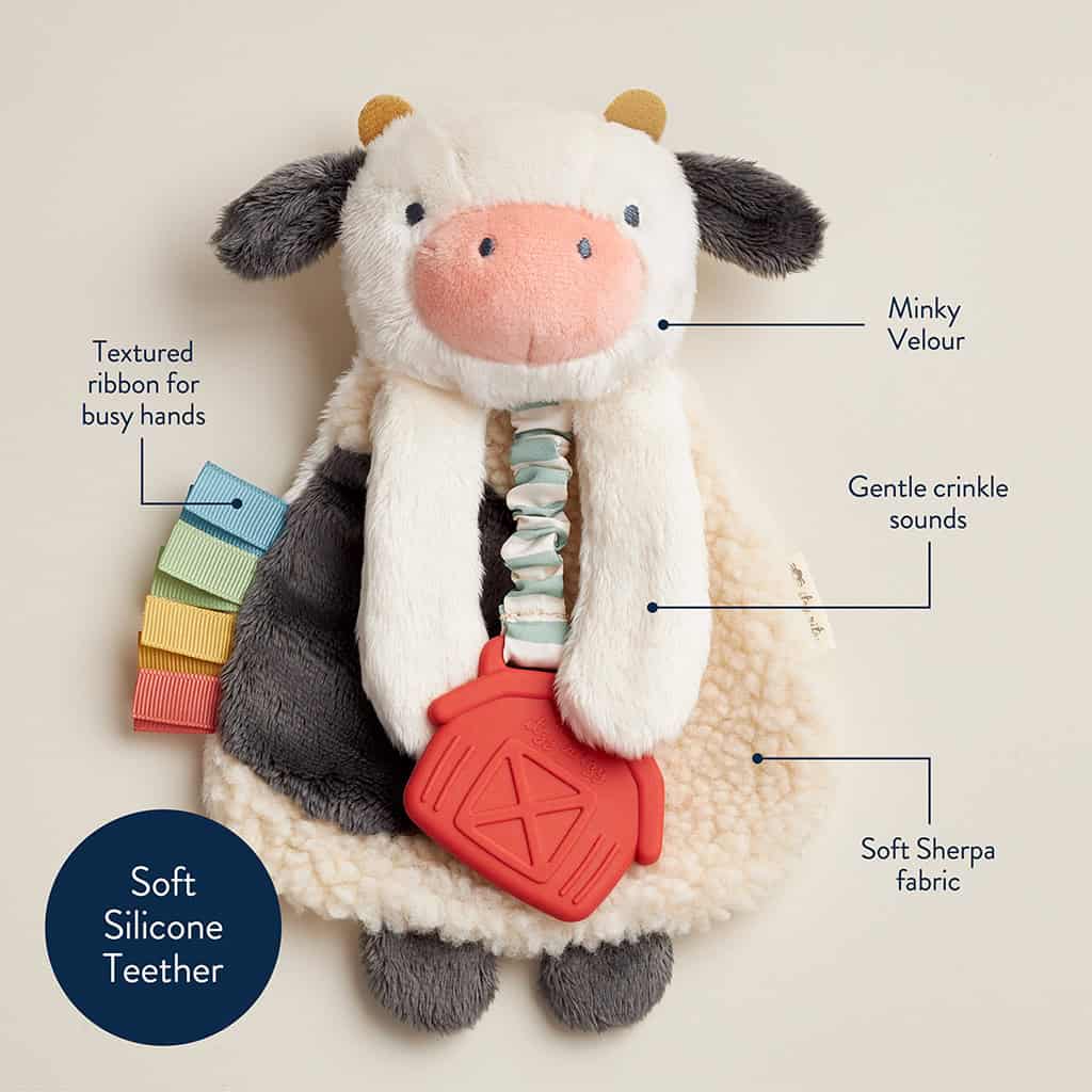 231130_Itzy_Lovey_Cow_Digital_Shelf_Template A stuffed cow toy with a textured ribbon, minky velour, gentle crinkle sounds, soft Sherpa fabric, and a soft silicone teether. Labels point to each feature.