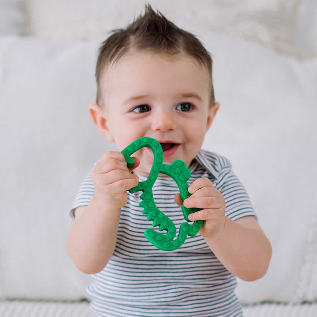 A baby is holding a green crocodile toy.
