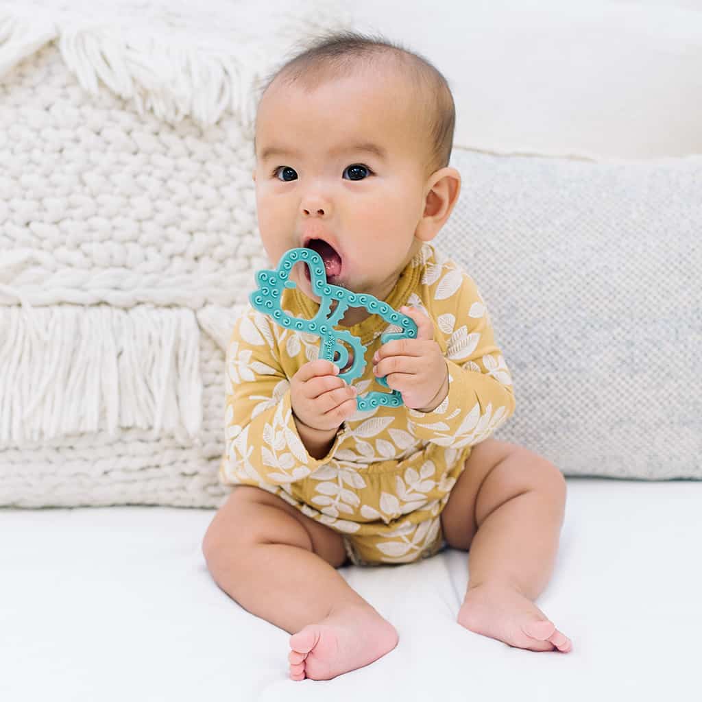 A baby is sitting on a bed eating a toy.