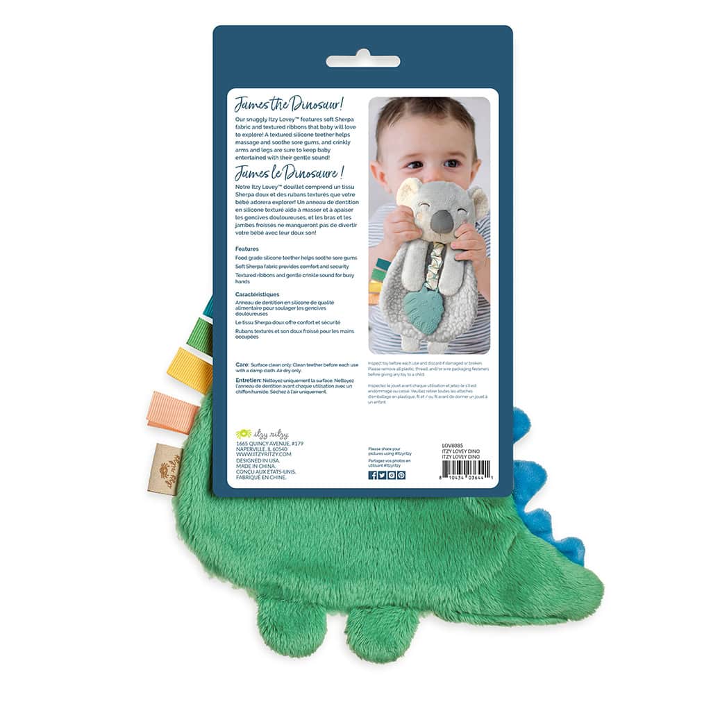 itzy-ritzy-lov8085-itzy-lovey-green-dino-2 Packaging of a green plush dinosaur toy with a photo of a baby hugging the toy on the back. The text describes the toy's features, safety information, and washing instructions in multiple languages.
