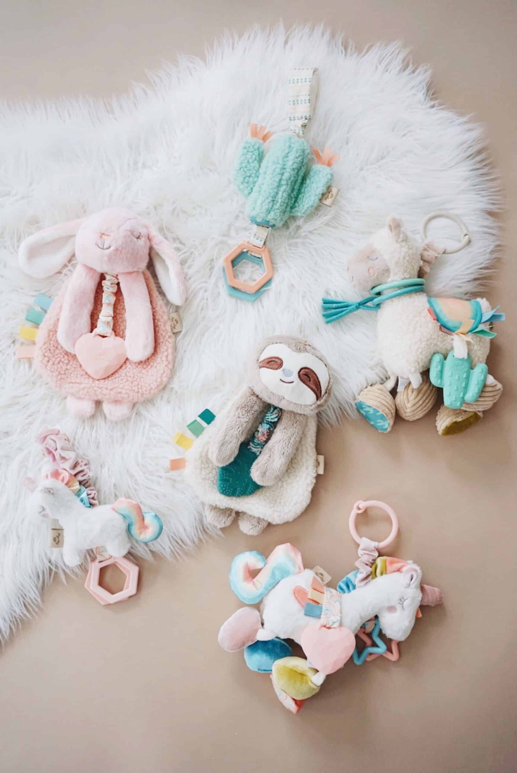 Processed with VSCO with a6 preset A variety of colorful plush baby toys including a pink rabbit, green sloth, llama, and unicorn are laid out on a white, furry surface.