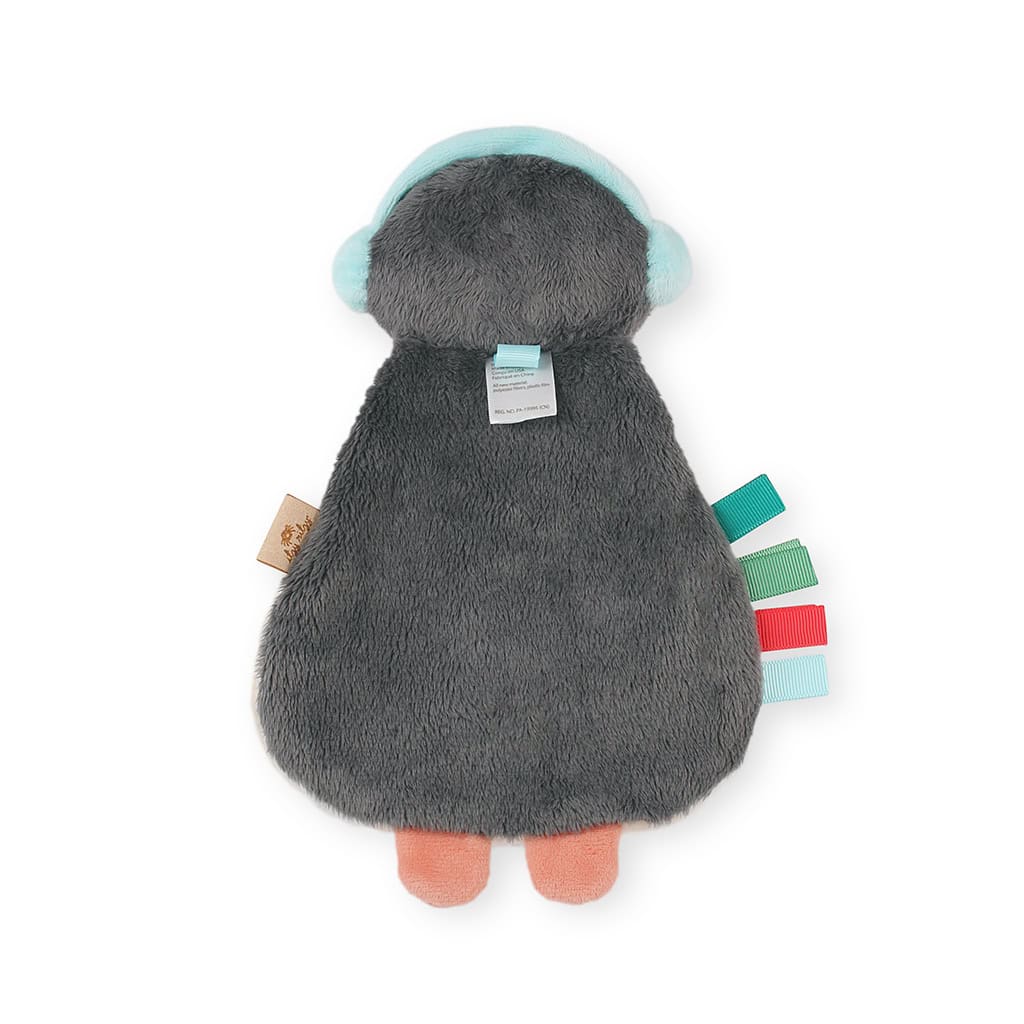 itzy-ritzy-lov8503-itzy-lovey-holiday-north-the-penguin-2 A plush toy with a grey furry body, blue head, orange feet, and multi-colored fabric tags on the side. The tag attached to the head is visible.
