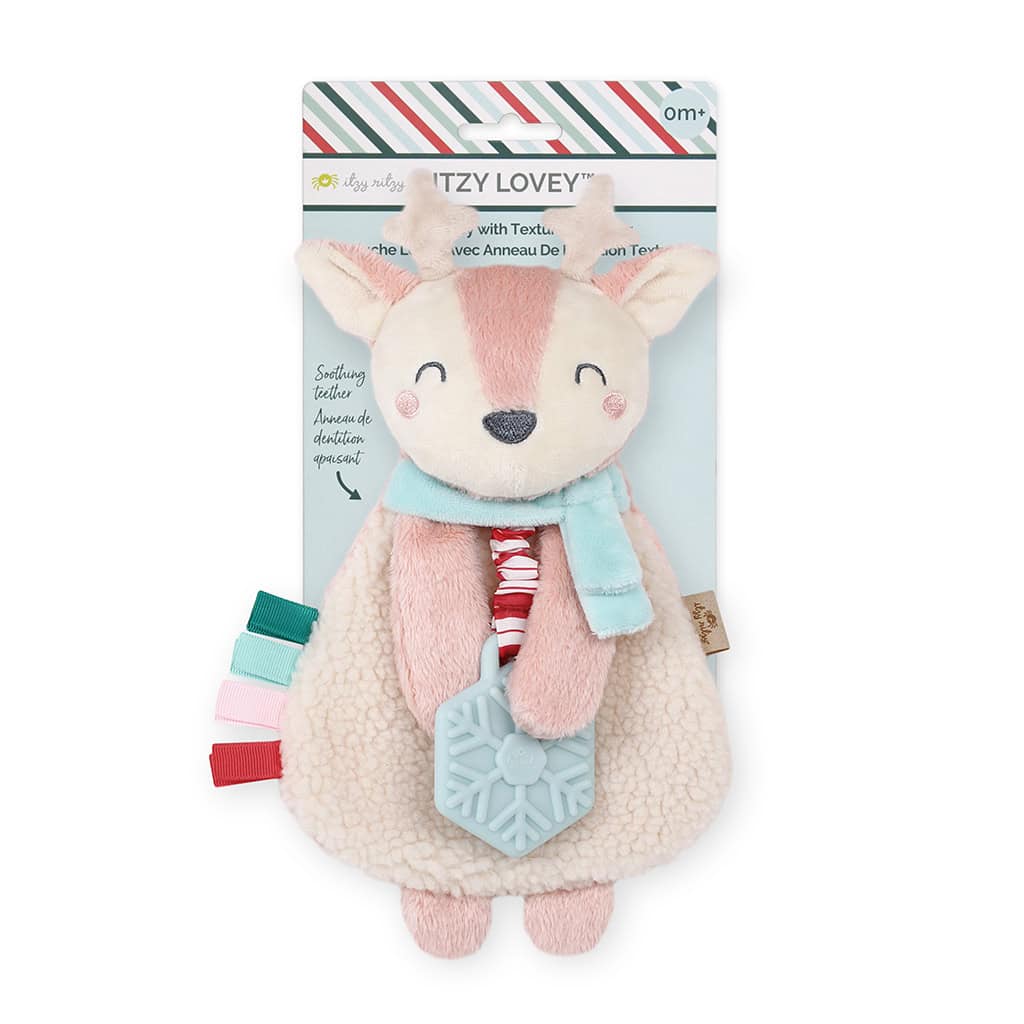 itzy-ritzy-lov8505-itzy-lovey-holiday-holly-the-reindeer-pink-2 A plush toy with a fox design, holding a blue teething ring, adorned with colorful tags and a striped scarf, in packaging labeled "Itzy Lovey.