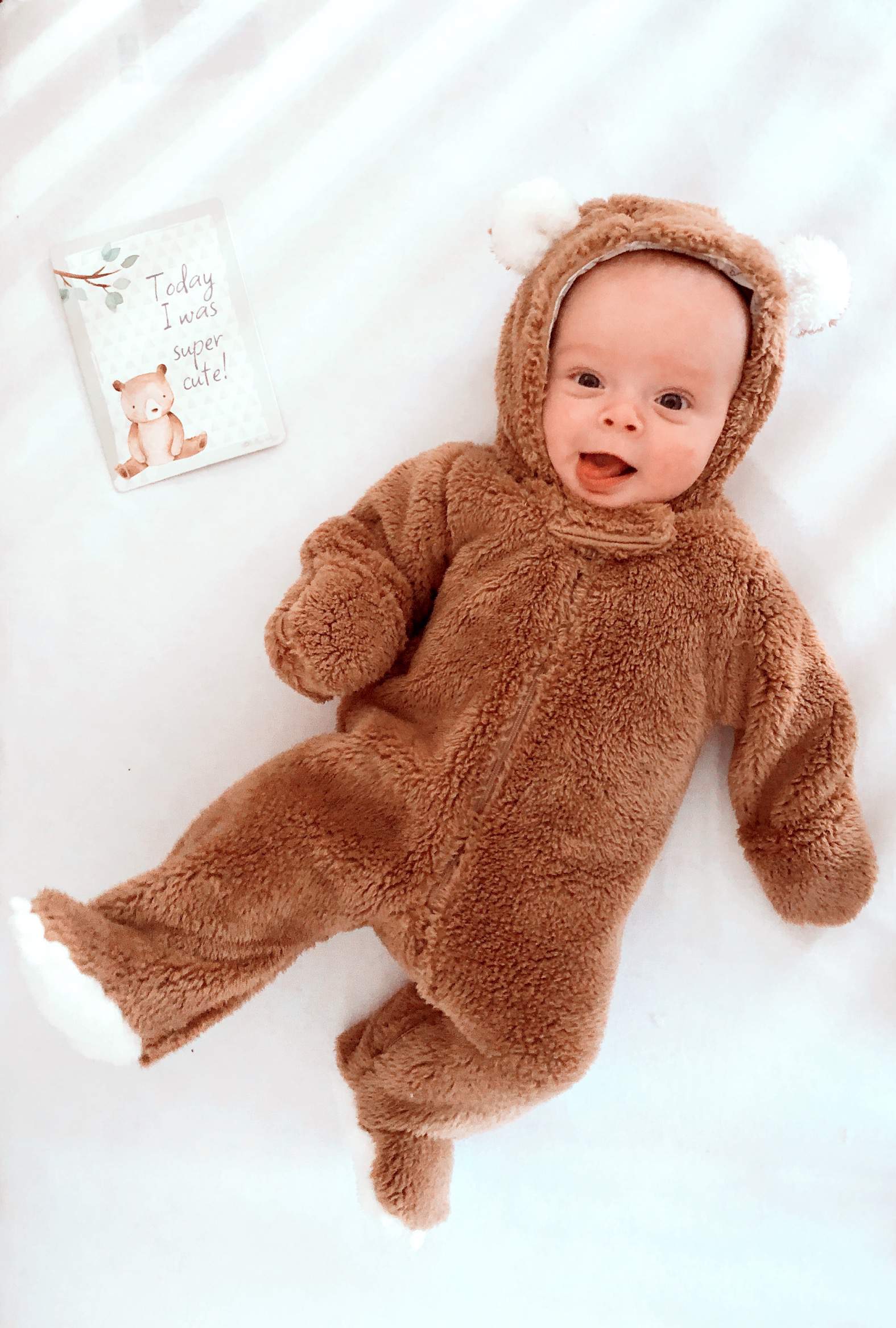 itzy-ritzy-mc8383-itzy-moments-woodland A baby in a bear costume laying on a bed.
