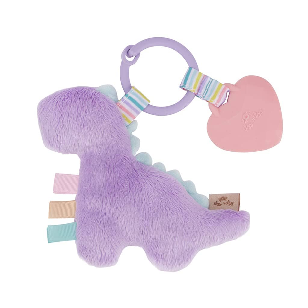 itzy ritzy pal lilac dino (2) A Itzy Ritzy - Itzy Pal - Plush Pal infant toy with a silicone teether in the shape of a purple dinosaur, with a ring and a pink heart attached, isolated on a white background.