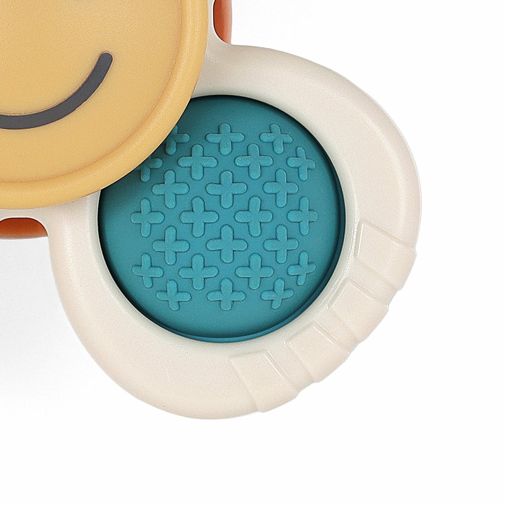 itzy-ritzy-spin8547-itzy-pop-&-whirl-smile-_4 Close-up view of a baby teething toy with two ring handles. One handle is blue with a textured surface, and the other is beige with a smooth surface and a brown smiley face.