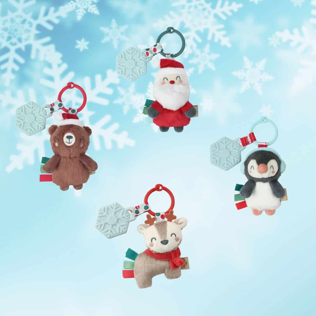 xr:d:DAE5NbWKUFI:2766,j:33472065718,t:22082221 Four Itzy Ritzy - Itzy Pal - Plush Pal Infant Toy with Silicone Teether keychains shaped like santa claus, a bear, a penguin, and a deer against a snowy background with snowflakes.