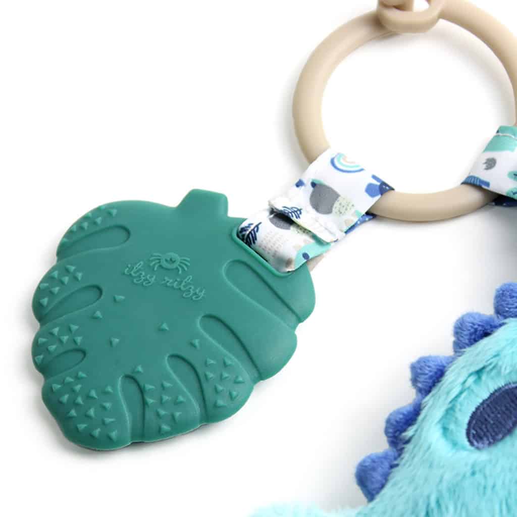 itzy-ritzy-tpl8449-itzy-pal-dino-3 A teal Itzy Ritzy - Itzy Pal - Plush Pal Infant Toy with Silicone Teether shaped like a mitten, attached to a patterned fabric strap and a plastic ring, isolated on a white background.